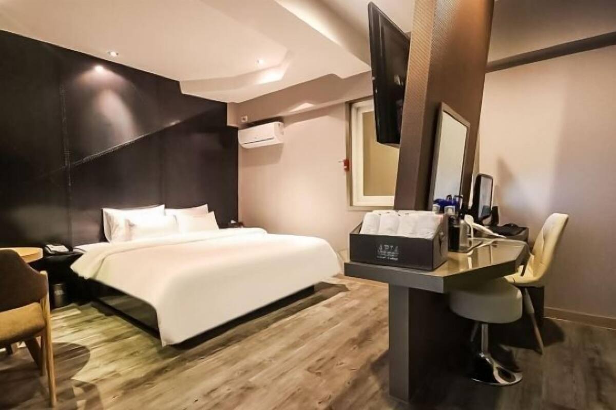 A hotel room with a bed, a desk with a chair, a TV, and a mirror.