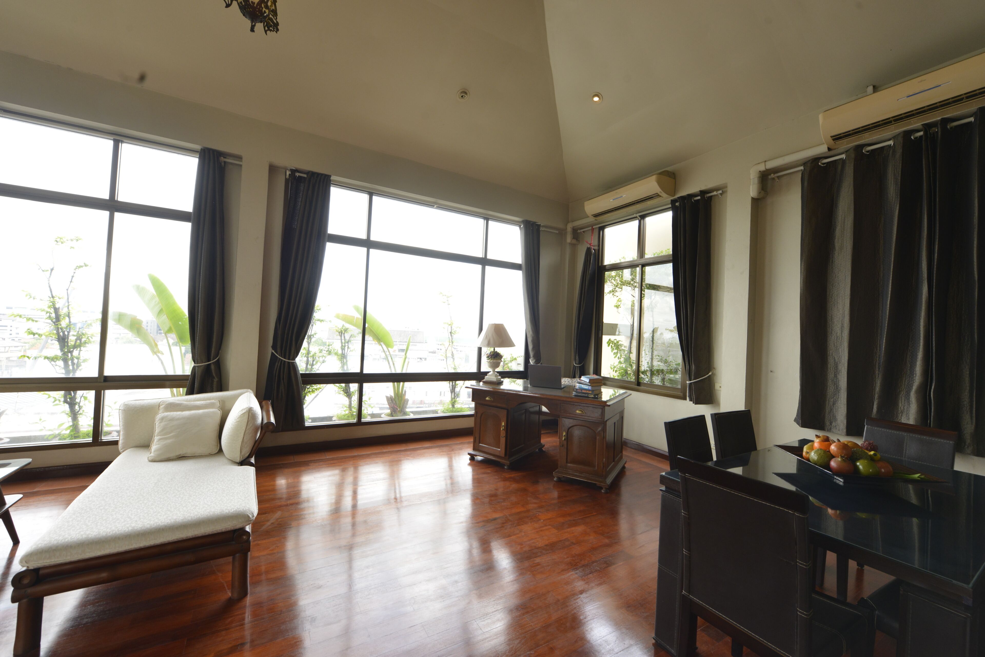 A spacious room with a bed, desk, and dining area, large windows with curtains, and an air conditioning unit.