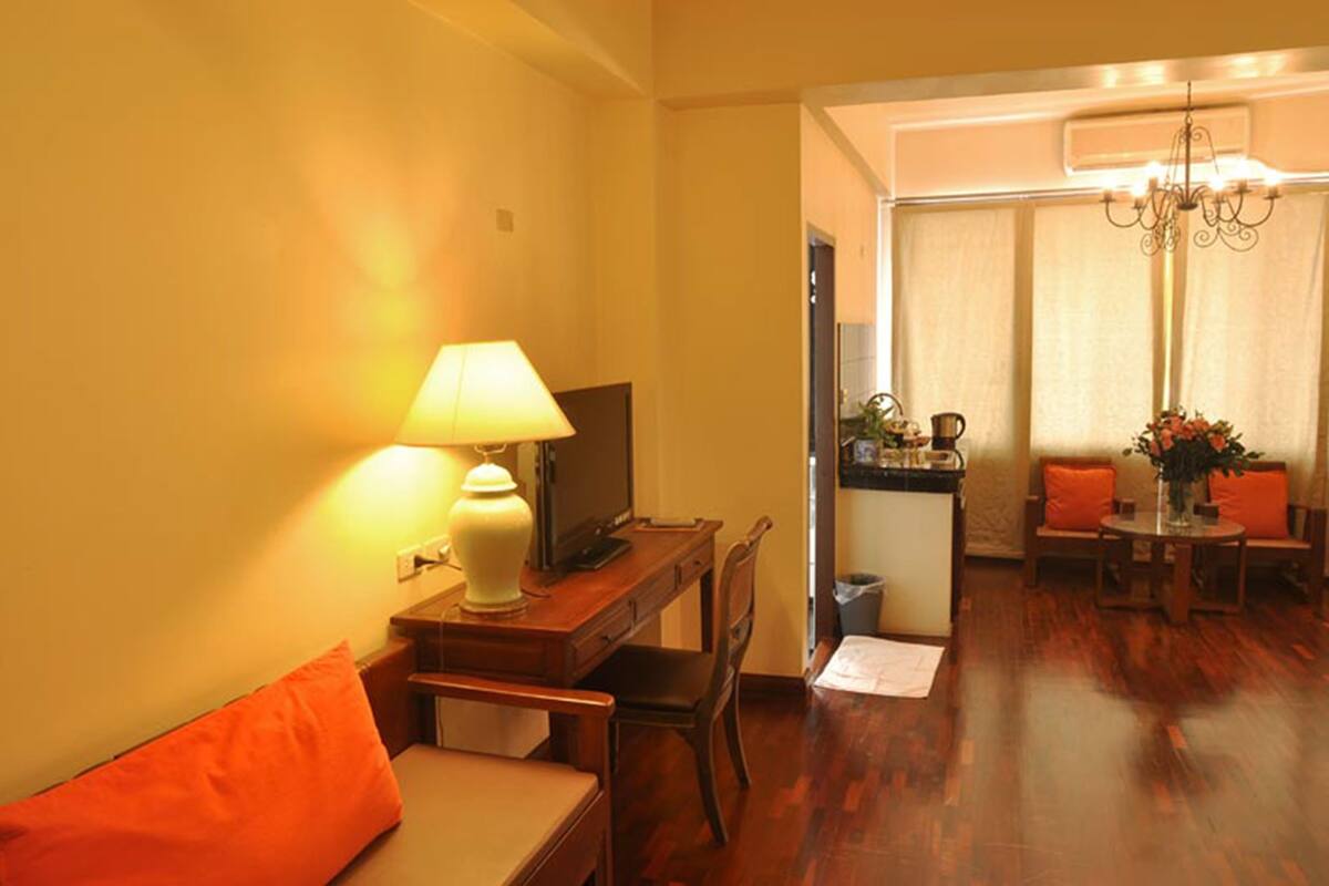 A cozy living room with a wooden desk, a comfortable sofa, a television, and a dining area with a table and chairs.
