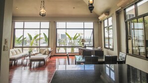 A spacious living room with a large window, a sofa, a dining table, and a kitchen area. - Sourire at Rattanakosin Island (Bangkok)