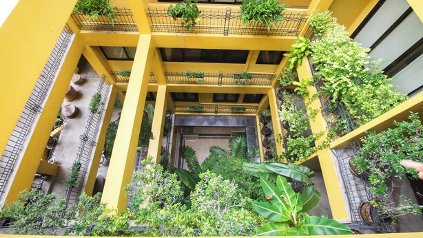 A multi-level atrium with yellow walls, multiple balconies with plants, and a central open space with potted plants. - Sourire at Rattanakosin Island (Bangkok)