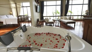 A spacious room with a large window, a bathtub with rose petals, a bed, and a seating area. - Sourire at Rattanakosin Island (Bangkok)