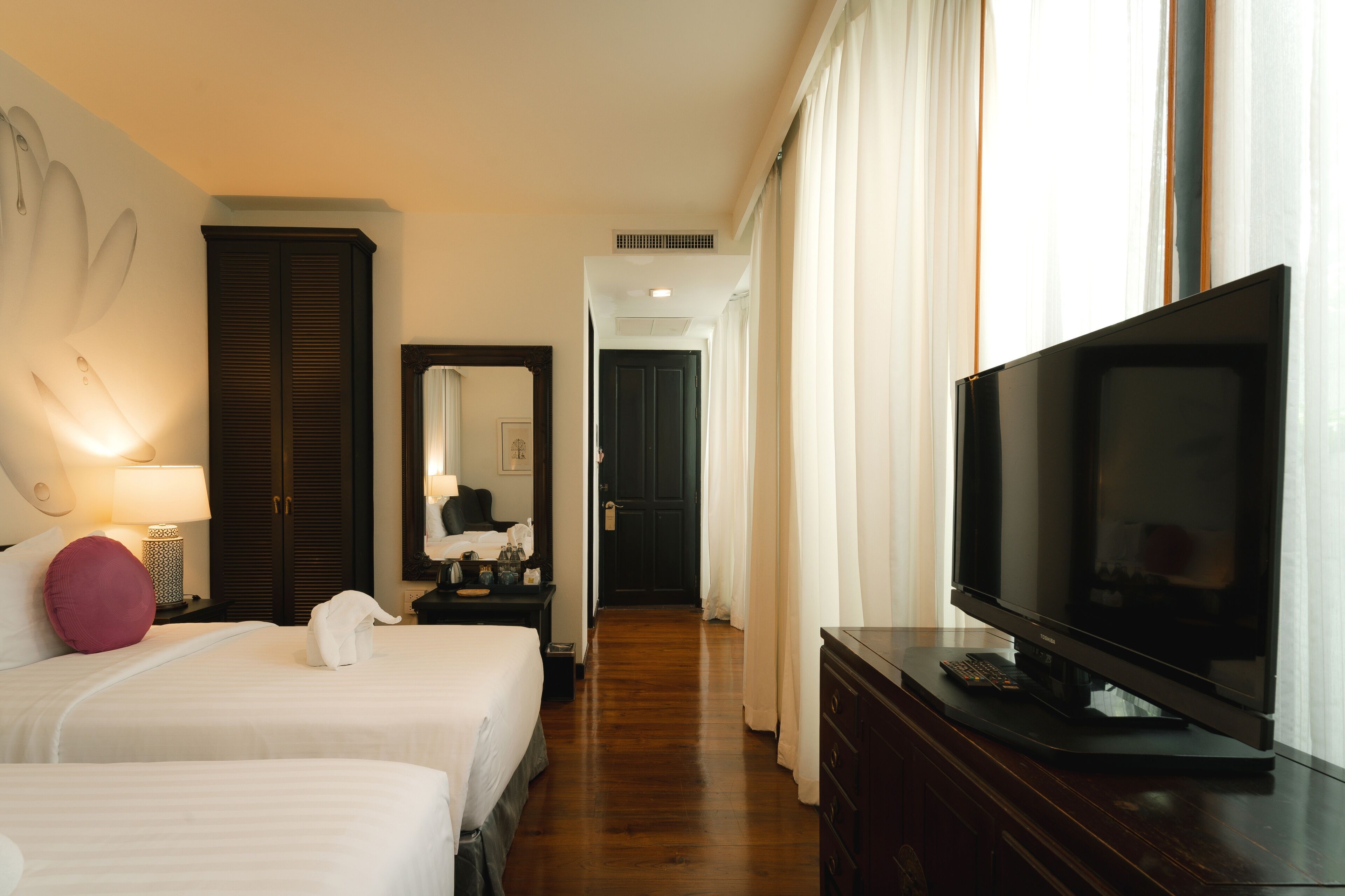 Habitación de hotel con dos camas, televisión, cómoda y un pasillo que conduce a una puerta.