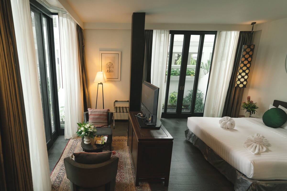 A hotel room with a bed, a TV, a desk with a lamp, and a view of the outdoors.
