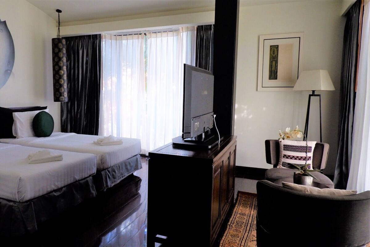 A hotel room with two beds, a TV, a desk, a chair, and a window with curtains.