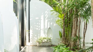Un sendero estrecho con un muro blanco a un lado y una jardinera de concreto con plantas al otro.