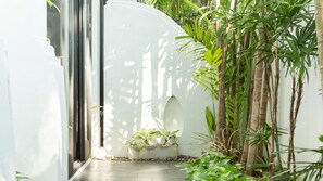Un sendero estrecho con un muro blanco a un lado y una jardinera de concreto con plantas al otro.