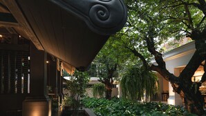 Un patio con fuente de agua, abundante vegetación y una columna arquitectónica de estilo clásico.