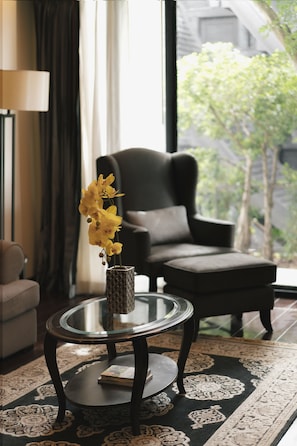 Un salón moderno con una mesa de centro de vidrio, un sillón oscuro y un jarrón con flores amarillas.