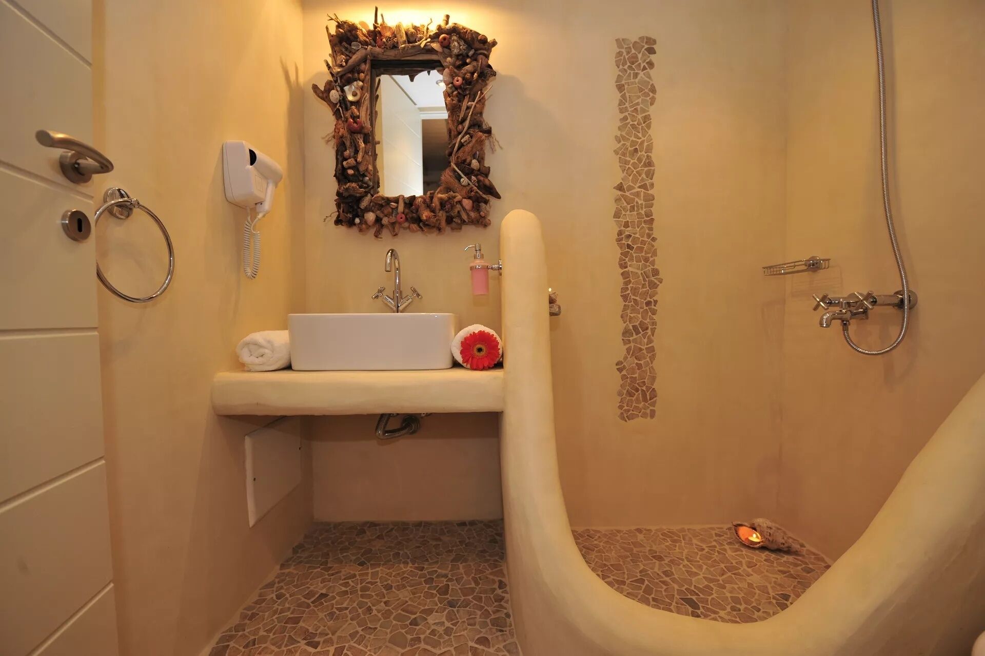 A bathroom with a stone-tiled floor, a white sink, a mirror with a rustic frame, a shower, and a towel rack.