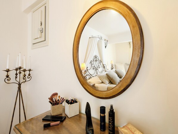 A bedroom with a round mirror, bedside table with makeup and toiletries, and a bed with a canopy. - Villa Isabella Studios & Suites (Paros)