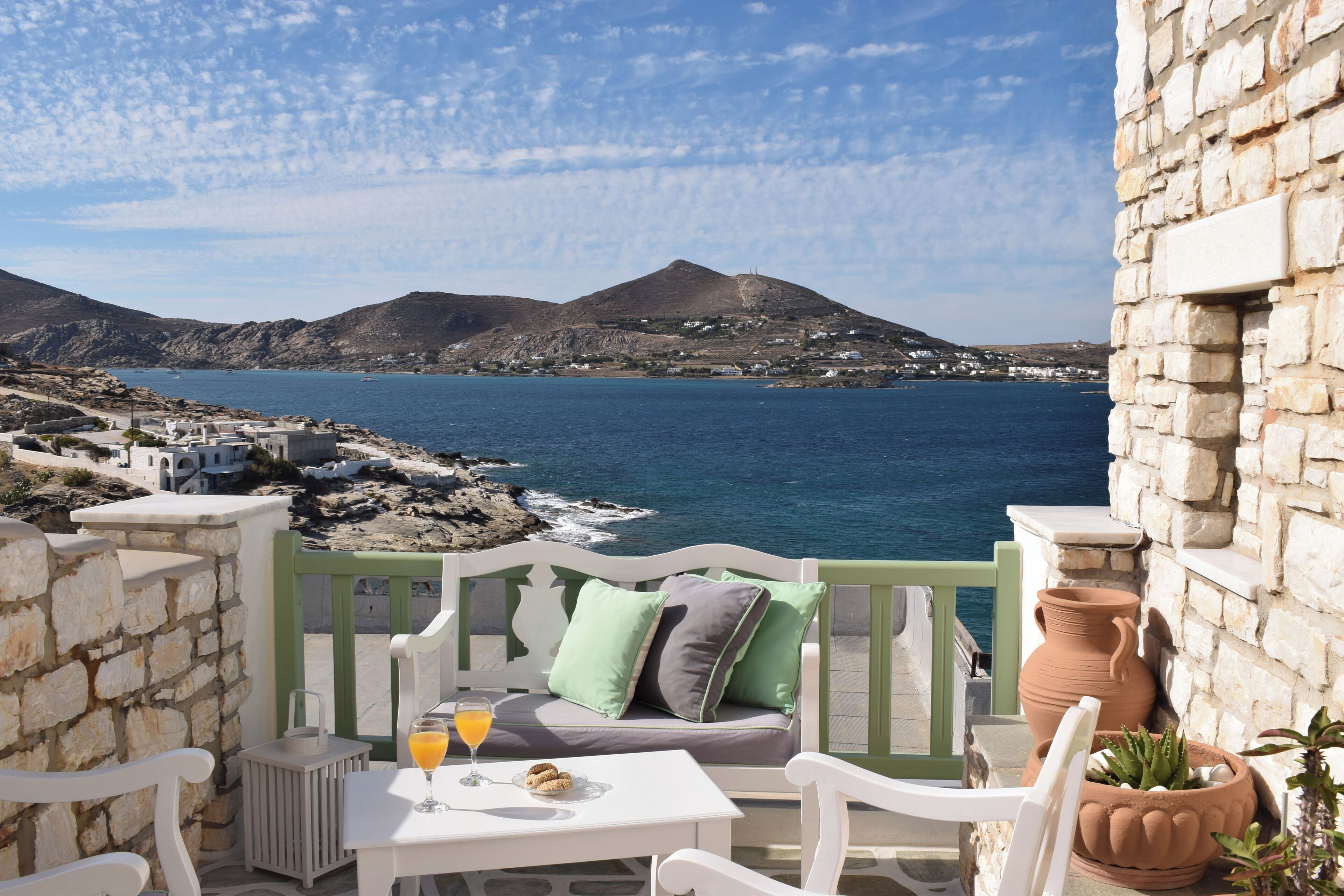 A balcony with a table, chairs, and a view of the sea and mountains.