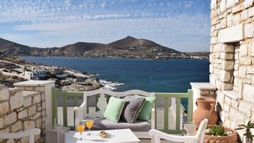 A balcony with a table, chairs, and a view of the sea and mountains.