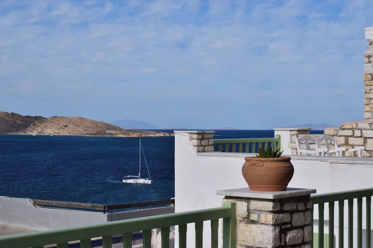 A coastal view with a sailboat on the water, a stone wall, and a potted plant.