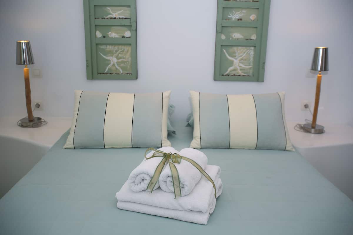 A neatly made bed with two pillows, a pair of folded towels, and two wall-mounted lamps.