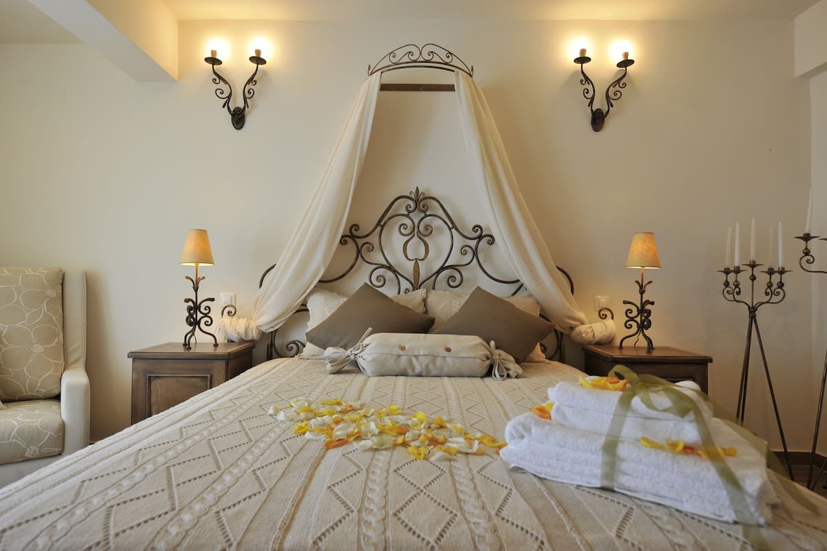 A bedroom with a canopy bed, two bedside tables with lamps, a chair, and a candelabra.
