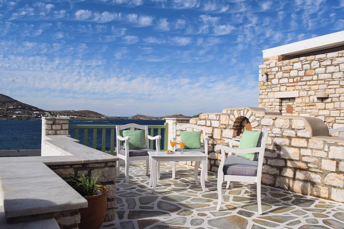 A stone-floored patio with white furniture and a view of the sea.