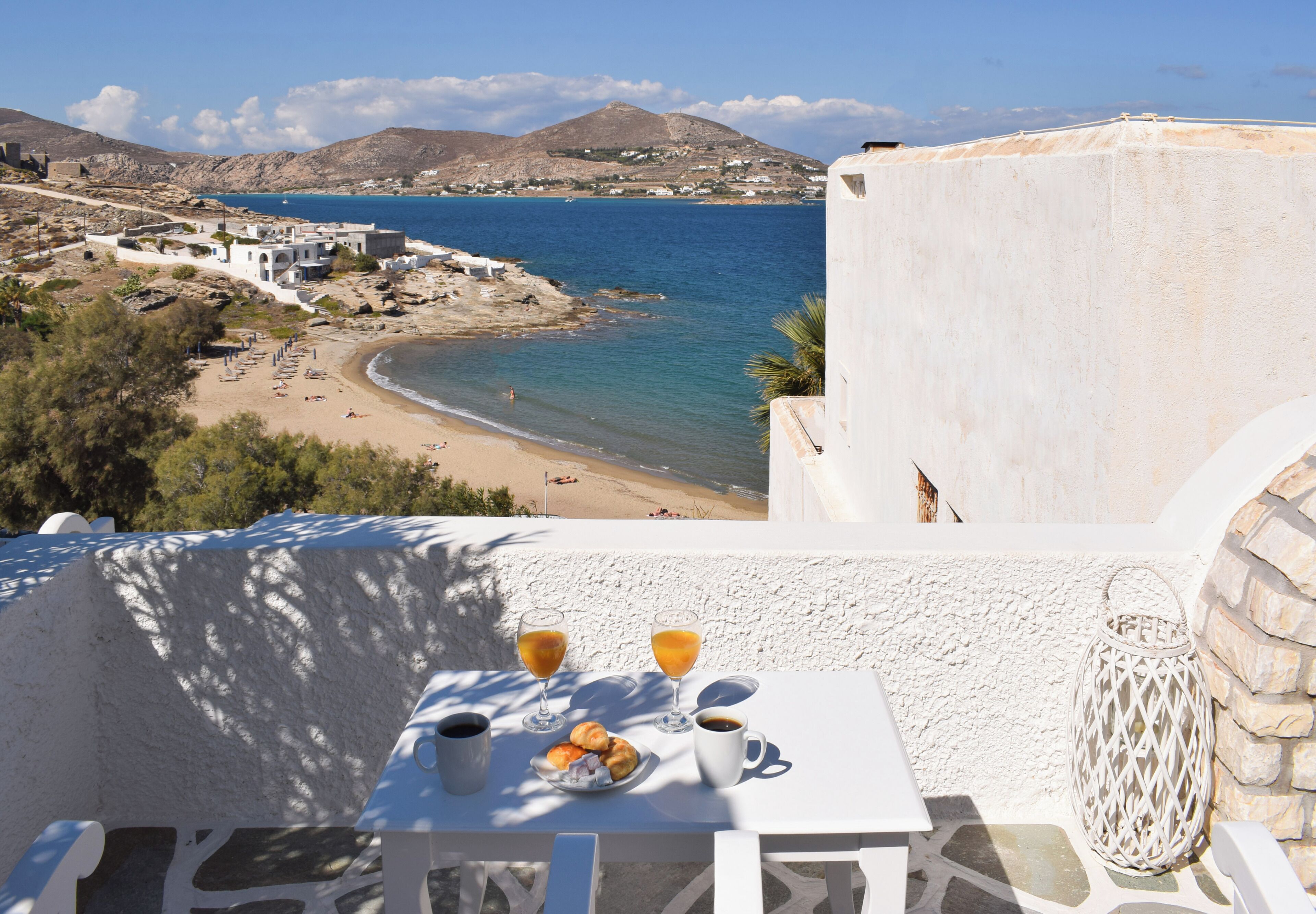 A table with breakfast items and a view of a beach and sea.