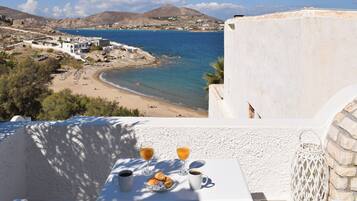 A table with breakfast items and a view of a beach and sea.