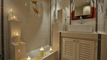 Un baño moderno con bañera, lavabo y ducha. Hay velas y pétalos de flores sobre la bañera.