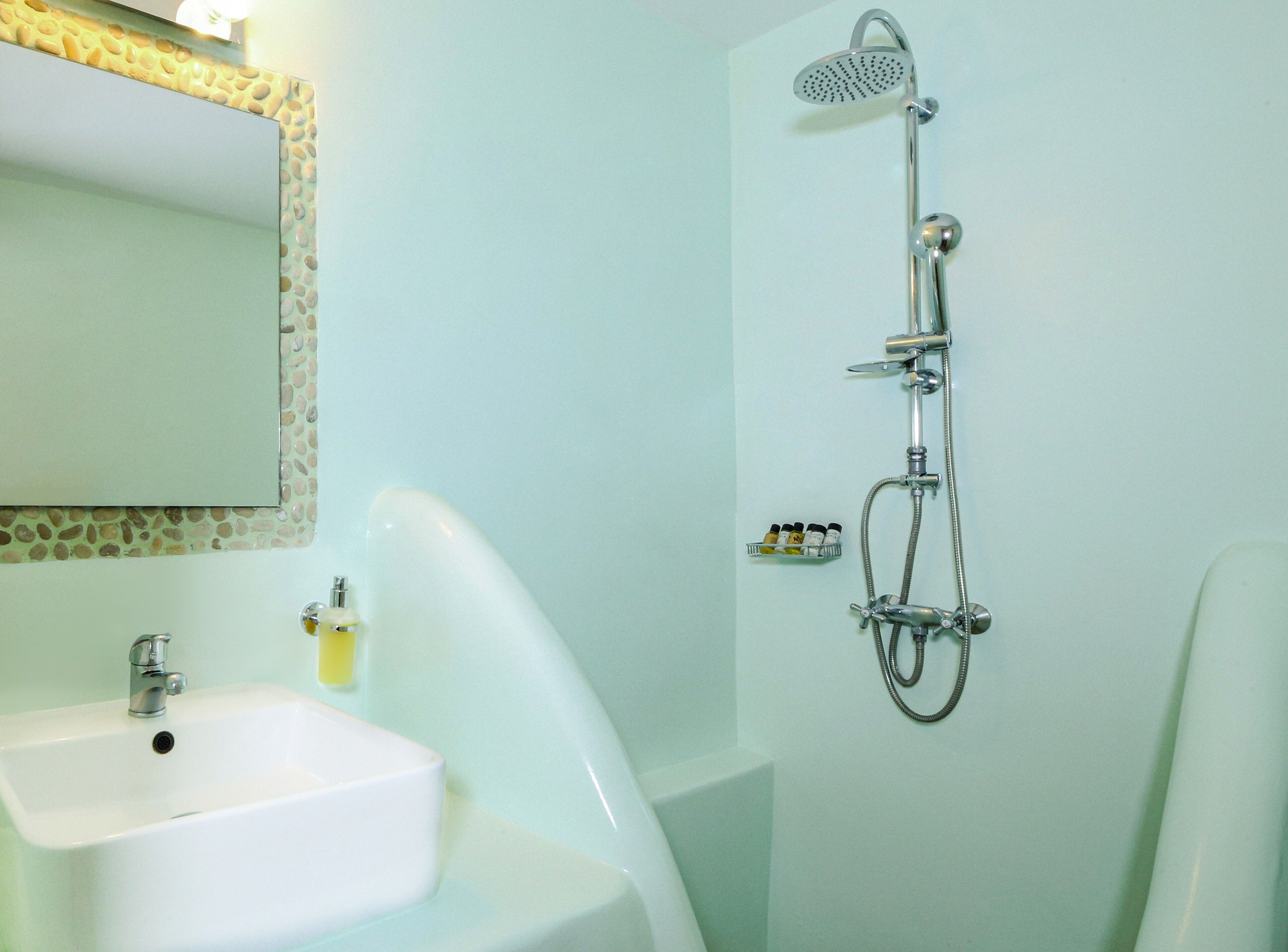 Une salle de bain avec un lavabo blanc, un miroir doté d’un cadre décoratif et une douche équipée d’un pommeau de douche à main.