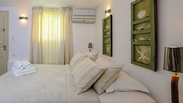 A neatly made bed with pillows and folded towels, a wall-mounted air conditioner, and a framed picture with shells.