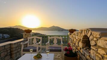 A terrace with a table set for two, a stone wall, and a view of the sea at sunset.