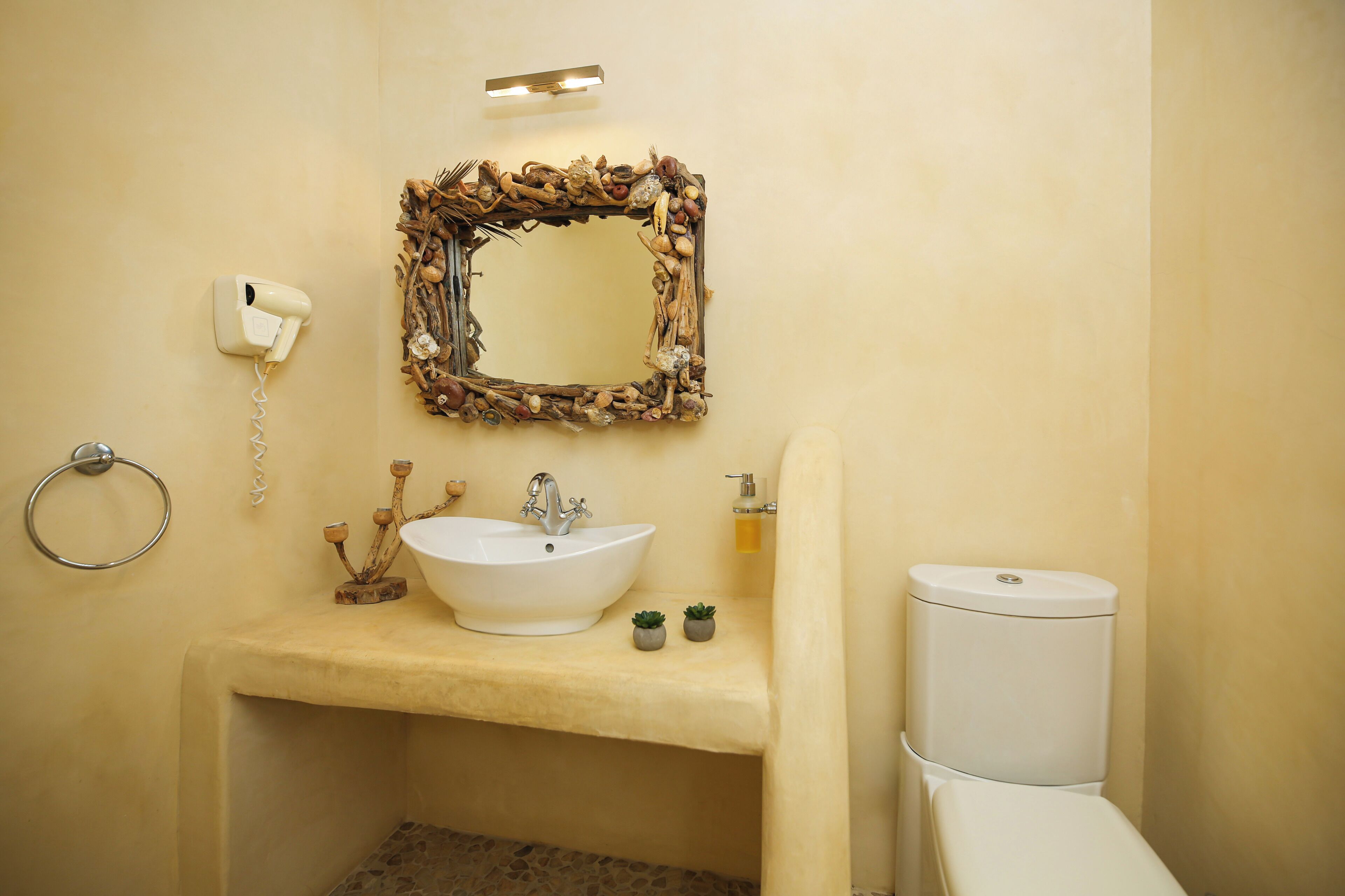 A bathroom with a white sink, a toilet, a mirror with a natural frame, a hairdryer, and a ring light.