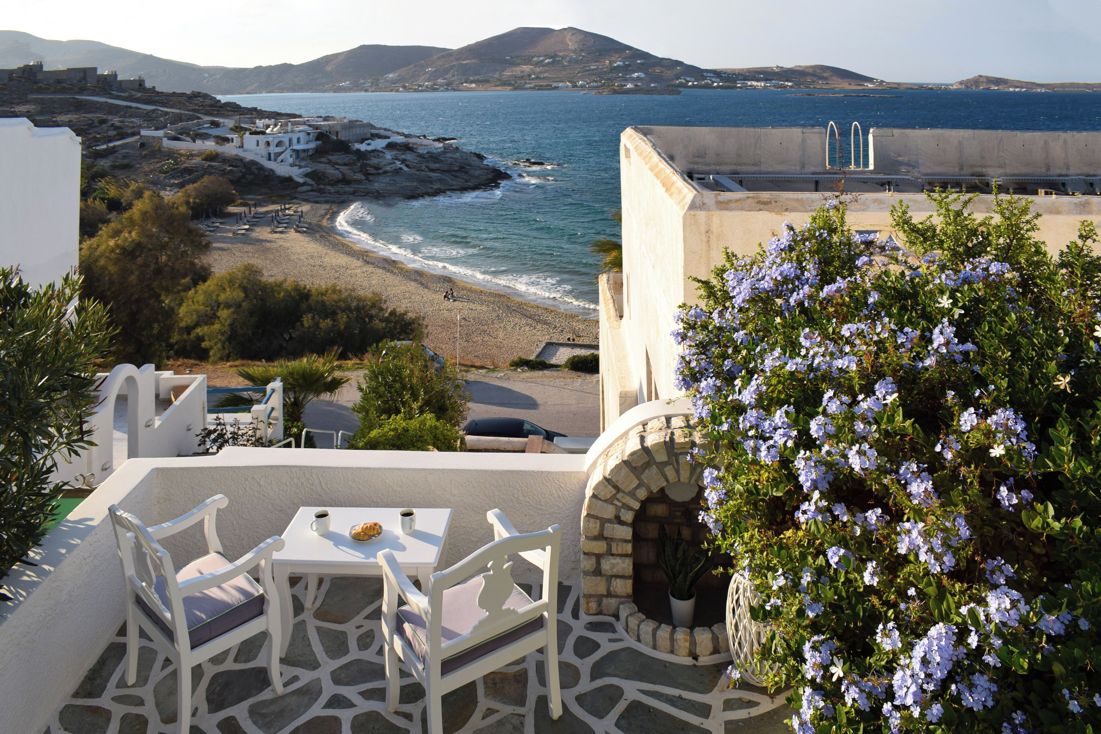 Eine Terrasse mit weißer Möbel, einem Steinofen und Blick auf das Meer und entfernte Gebäude.