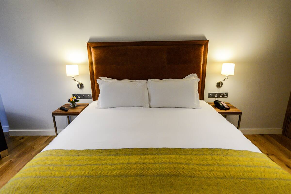 A hotel room with a large bed, two bedside tables, a wooden headboard, and two wall-mounted lamps.