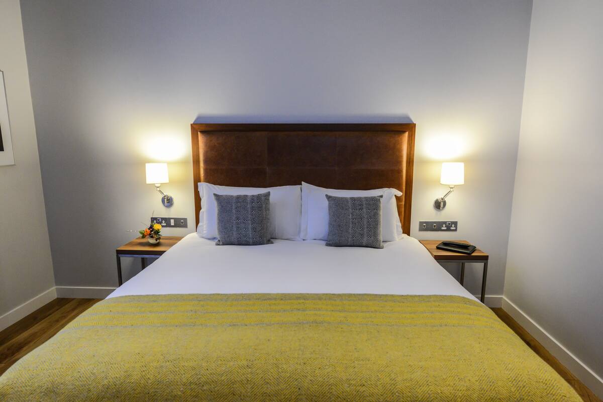 A neatly made bed with a wooden headboard, two bedside lamps, and a small table with a vase of flowers.