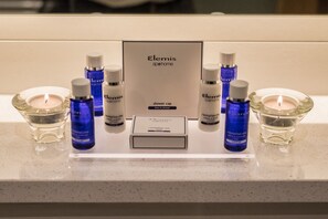 A bathroom vanity with Elemis shower cap and lotion bottles, a candle, and a sign. - Premier Suites Dublin Ballsbridge (Dublin)