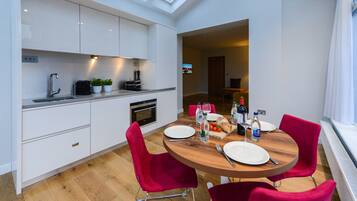 A modern kitchen with white cabinets, a wooden dining table, and red chairs.
