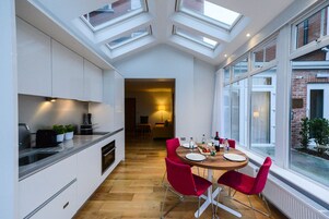 A modern kitchen with skylights, a dining area with red chairs, and a view of a brick building.