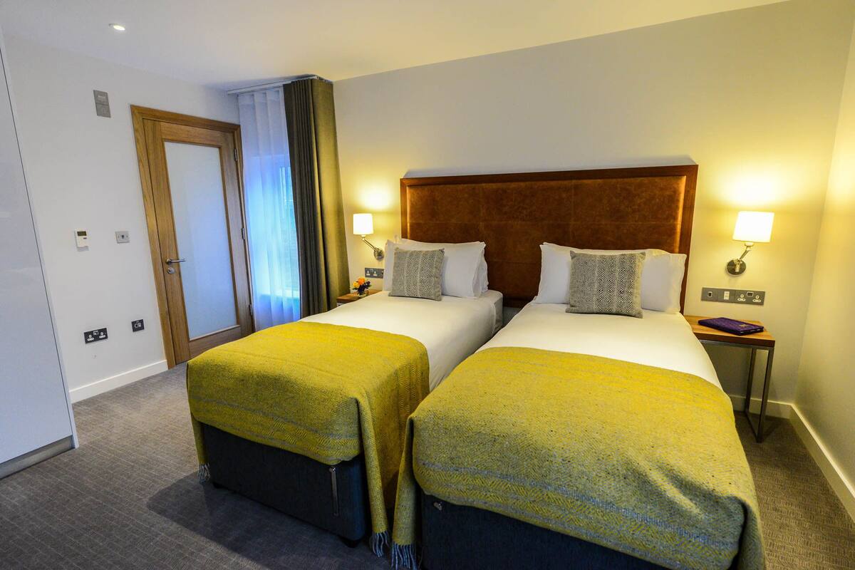 A hotel room with two beds, a wooden headboard, bedside lamps, and a small table with a flower vase.