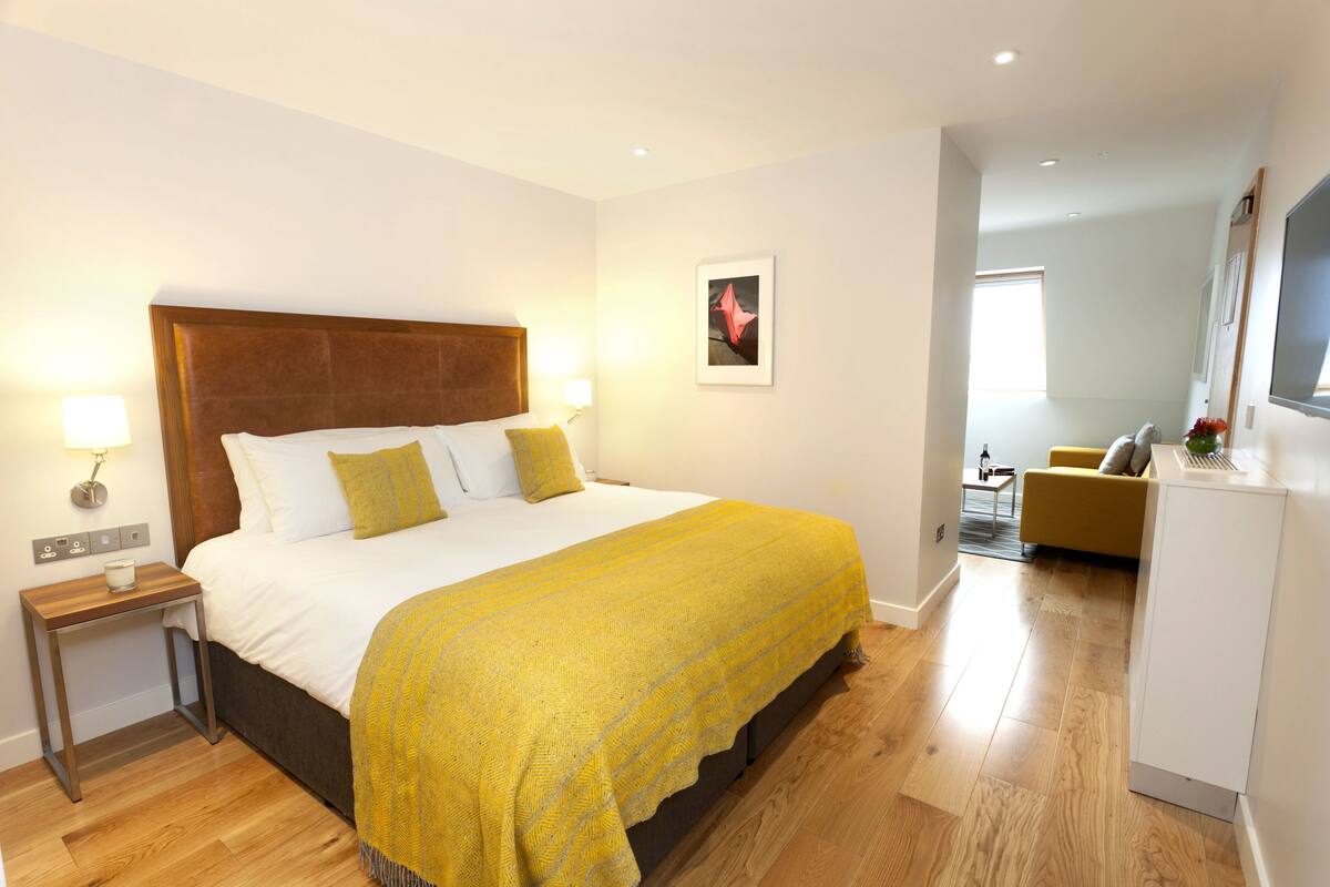 A hotel room with a large bed, bedside tables, a small desk, a sofa, and a TV.