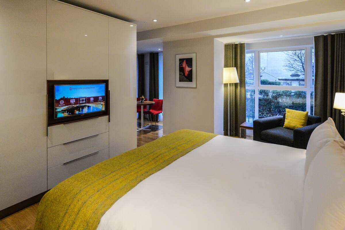 A hotel room with a bed, a TV, a desk, and a window with curtains.