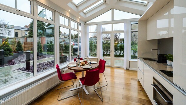 Una cocina moderna con ventanas amplias, un comedor con sillas rojas y vistas al jardín.