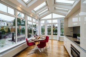 A modern kitchen with large windows, a dining area with red chairs, and a view of the garden. - Premier Suites Dublin Ballsbridge (Dublin)