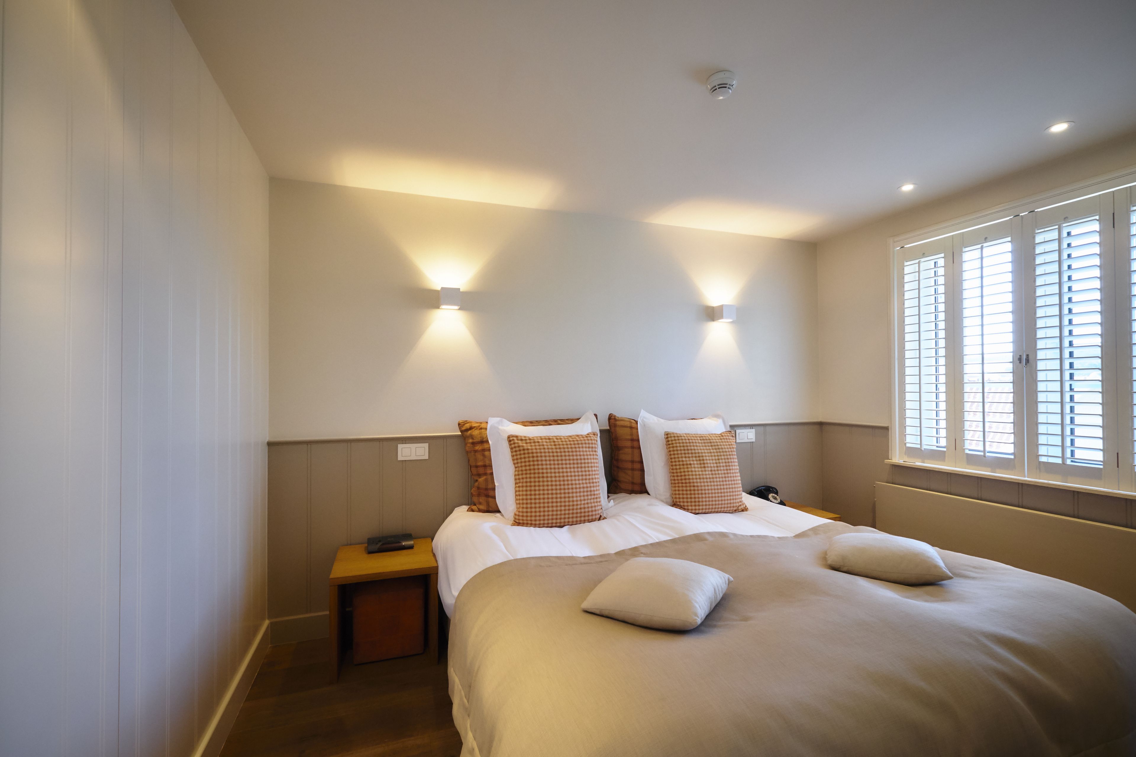 Un dormitorio con una cama grande, dos mesitas de noche e iluminación en la pared.