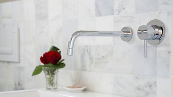 Ein modernes Badezimmer mit einer Wand aus weißem Marmorfliesen, einem chromfarbenen Wasserhahn und einer roten Rose in einer klaren Glasvase.