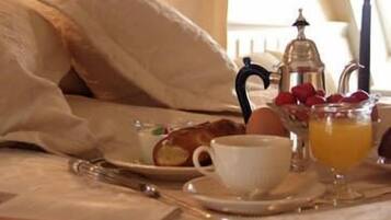 Ein ordentlich gemachtes Bett mit Kissen, ein Tablett mit Frühstücksartikeln, darunter Eier, eine Tasse und ein Glas Orangensaft.