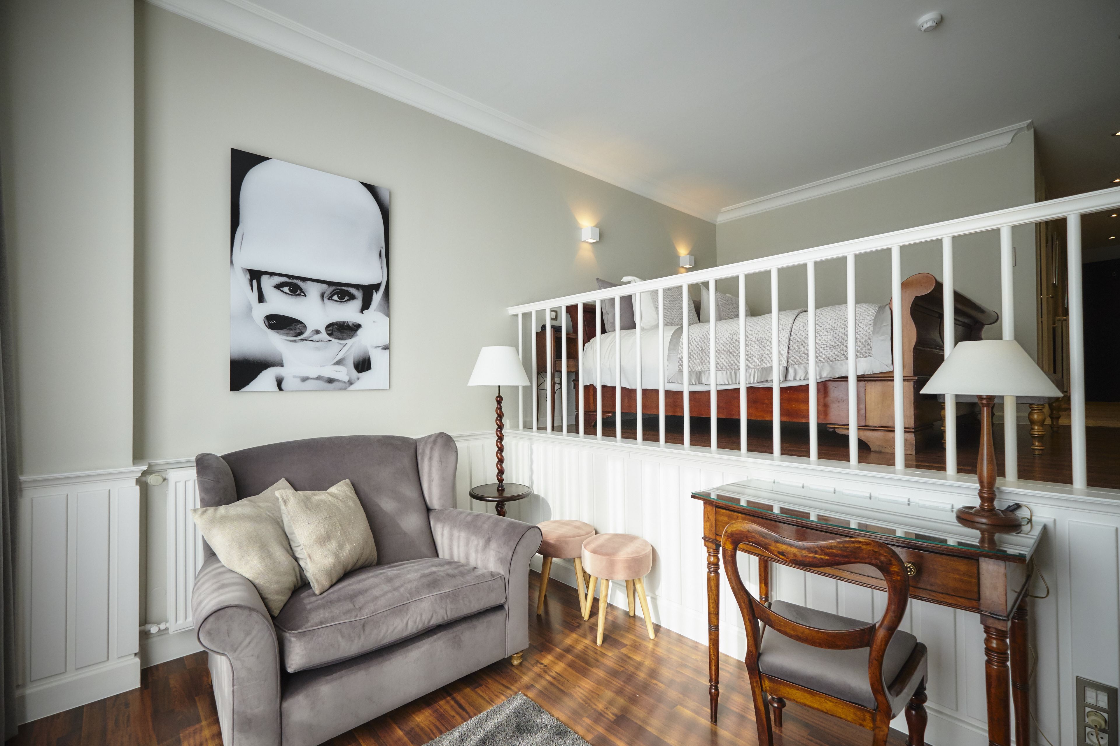 A living room with a grey sofa, two small stools, a wooden desk, and a white railing.