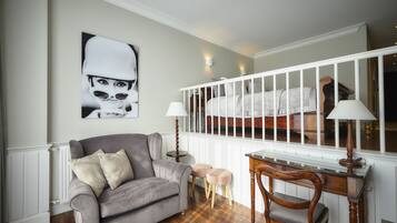 A living room with a grey sofa, two small stools, a wooden desk, and a white railing.