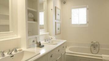 A modern bathroom with two sinks, a large mirror, and a bathtub.