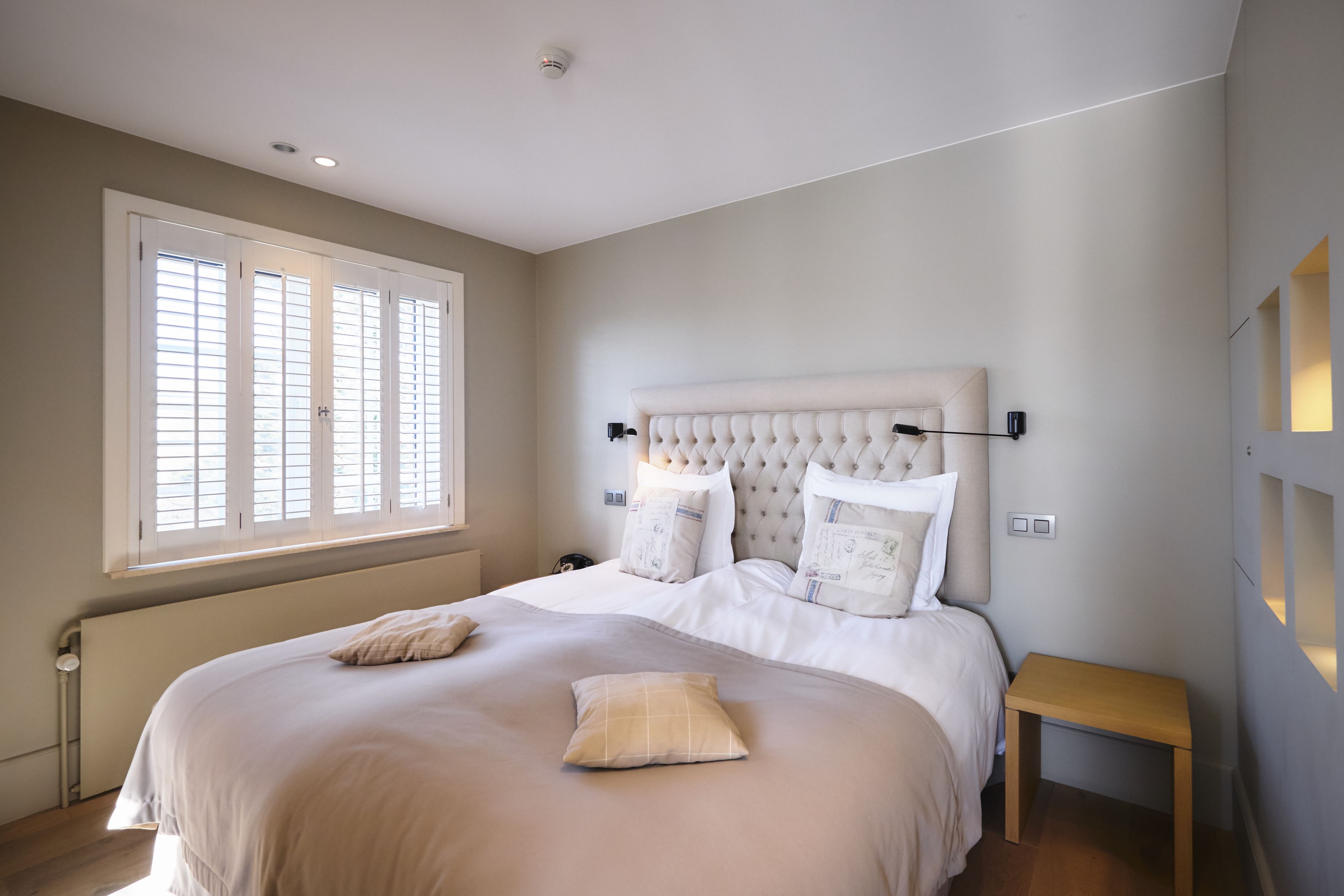 A bedroom with a large bed, a bedside table, and a window with blinds.