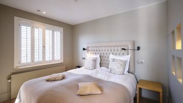 A bedroom with a large bed, a bedside table, and a window with blinds.