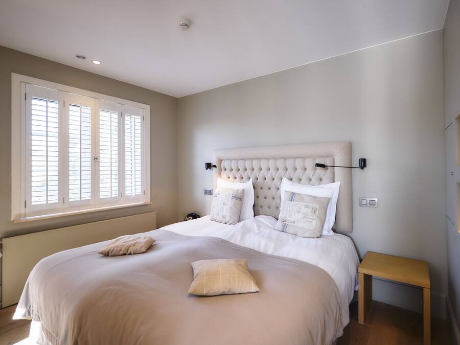A bedroom with a large bed, a bedside table, and a window with blinds.