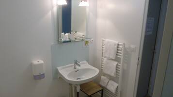 A small bathroom with a white sink, a mirror, a towel rack, and a small wooden stool.
