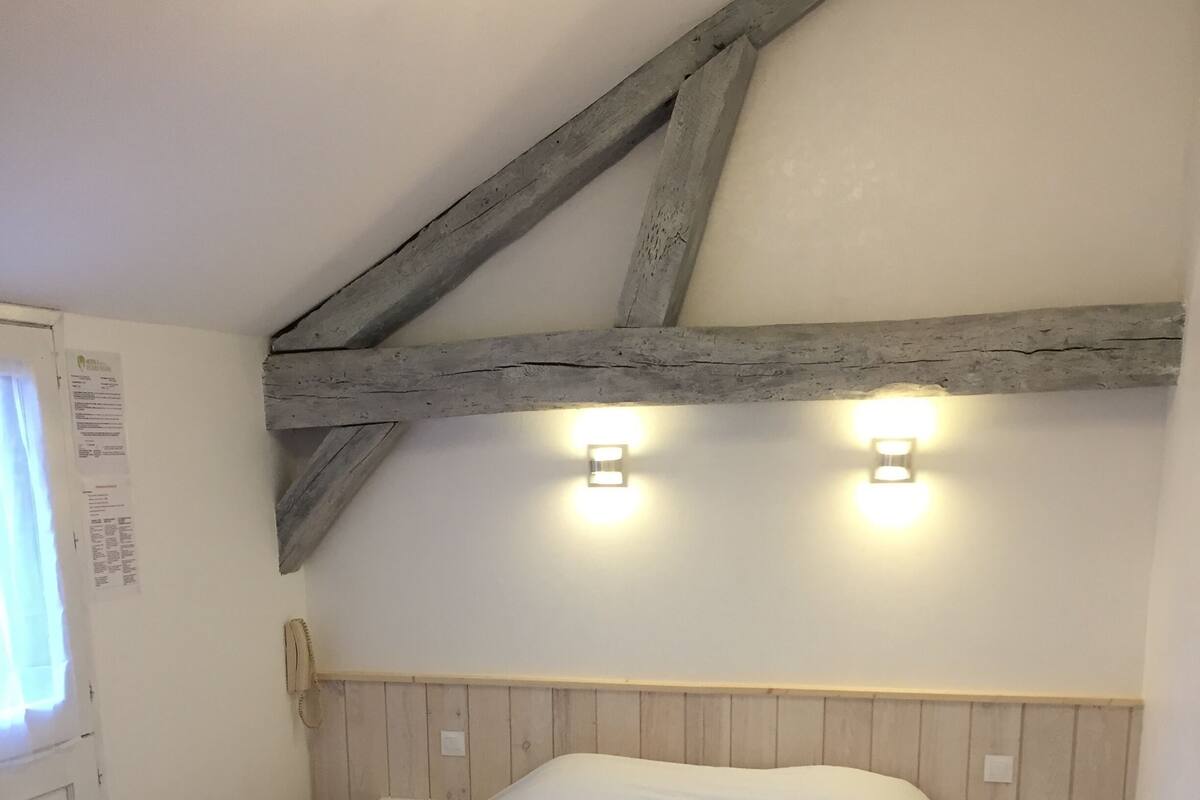 A bedroom with a wooden ceiling, a bed, two bedside tables, and two wall-mounted lights.